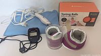 Group shot showing heating pad, controller, toning balls in container, stopwatch, wrist weights, and Merrithew box