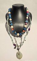 Full view of multi-strand beaded necklace on bust showing bead arrangement and pendant