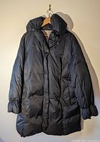 Full view of black long puffer coat on hanger showing hood, length and front closures