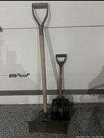 Both shovels standing against a garage door
