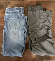 Blue denim jeans and grey pants laid flat on floor