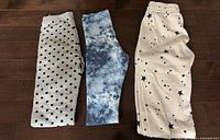 Three pairs girls pants laid flat: polka-dot leggings, tie-dye leggings, star-print sweatpants