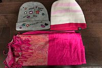 Grey embroidered beanie, pink striped beanie, pink paisley scarf laid flat