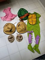 All items laid out: Ninja Turtle costume components, pink dress, four safari hats