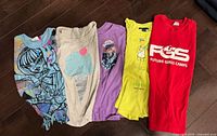 Five T-shirts laid out showing fronts and graphics