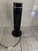 Front view of black tower heater with mesh grille and base