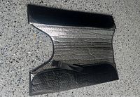 Foldable reflective windshield sunshade laid flat showing silver foil surface, black edges and elastic strap