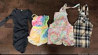 Four garments laid flat: black ruched dress, tie-dye tank & shorts set, tie-dye shortalls, plaid pinafore