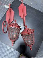 Pair of red metal wire-cage lantern wall candle sconces on black surface