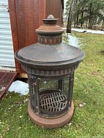 Front view of cylindrical metal chiminea showing mesh body, hinged door, pedestal base