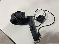 Fitbit smartwatch on charging stand with spare band and USB charger cable