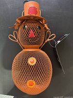 Front view of orange mesh pumpkin scarecrow bird feeder showing body, top hat, rope arms and attached tag