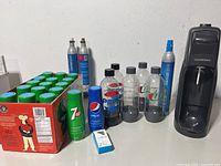 Complete lot showing SodaStream machine, CO2 cylinders, five bottles, Pepsi syrup bottle, and case of 16 7UP syrup bottles