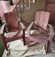 Two red plastic Adirondack chairs on floor covering