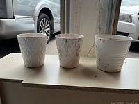 Three small white glass flower pots in a row showing distinct textures and signs of prior soil use