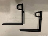 Two matching black metal curtain rod brackets shown flat to display shape and condition