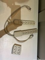 Two beige six-outlet power strips with cords and one six-outlet wall tap adapter on a white surface