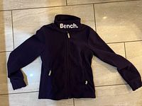 Full view of purple Bench fleece jacket laid flat showing front, collar logo, pockets