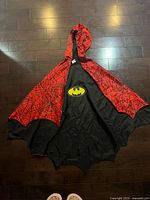 Cape laid out showing black Batman side with yellow emblem and red web hood lining