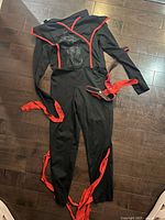 Full view of kids black ninja warrior costume laid flat showing jumpsuit, belt sash and eye mask