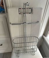 Front view of chrome over-the-tank toilet paper holder showing dispensing arm and basket