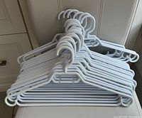 Stack of approximately 18 white plastic clothes hangers with strap notches