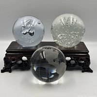 Front view of three glass paperweights on wooden stand