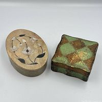Two lidded boxes side by side closed—oval stone with floral inlay and square green-gold painted box
