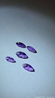Five marquise-cut purple gemstones on light background