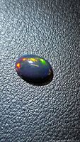 Front view of oval Ethiopian black opal cabochon on textured background showing play of color
