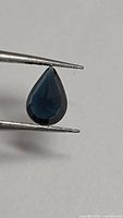 Pear cut blue spinel held in tweezers, front view