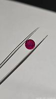 Round ruby held in tweezers showing overall size and color