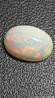 Oval cabochon opal showing strong play of color on black background