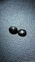 Both oval cabochon star diopsides on textured surface, showing four-ray star effect