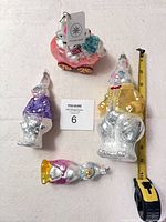 Front view of all four glass ornaments including Bunmobile, two standing rabbits, Mother Goose with measuring tape for scale