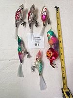 Group shot of six blown glass clip-on parrot ornaments next to measuring tape