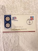 Front of coin cover showing two quarters, 50 State Quarters logo, Delaware labeling
