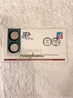 Front of sealed Pennsylvania coin cover showing two quarters, logo, dates, and text