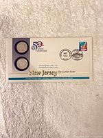 Front of sealed first day coin cover showing two quarters, 50 State Quarters logo, postmark and stamp