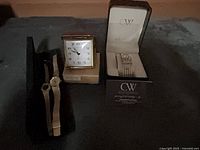 Overall lot view showing two gold-tone watches, square desk clock, and boxed CW watch