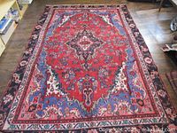 Full view of rug showing red field, blue corners, dark border, fringe
