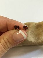 Pair of garnet stud earrings held between fingers, showing front view