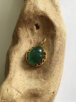 Front view of 14K gold pendant with green cabochon stone on wood prop