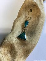 Front view of gold pendant with two green stones on driftwood