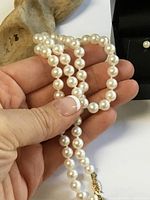 Hand holding strand of uniform white pearls showing clasp detail
