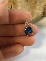 Earring held between fingers showing blue marquise stone and clear accents