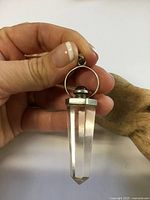 Pendant held in hand showing quartz point, silver cap, amethyst cabochon, bail