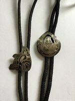 Front view of both bolo ties showing carved sterling slides and cords