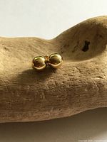Both gold-tone ball stud earrings displayed on wooden base