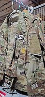Front view of several U.S. Army camouflage shirts showing name tape, rank patch, velcro panels